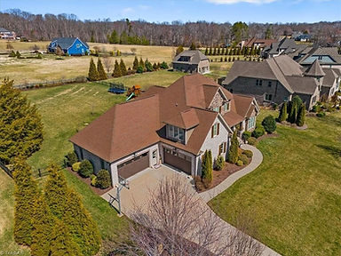 aeriel view of the exterior of a large brick and stone home with gabled rooflines, attached garage, covered front porch, and landscaped yard