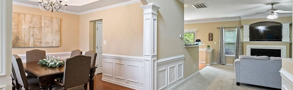 Open-concept interior featuring a formal dining room with wainscoting and chandelier flowing into a living area with fireplace, built-in shelving, and neutral finishes.