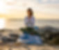 yoga-instructor-in-calming-pose-with-hand-in-prayer-sitting-on-rocks-infront-of-the-sea-in