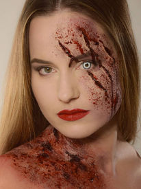 SFX Makeup, Woman with blonde hair wearing Halloween makeup. She has a white lens in one eye and fake blood running down one side of her face and one shoulder.