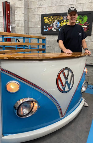 Man standing next to TV stand made from the front end of a VW Bus.