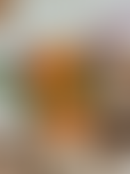 Vase of vibrant orange gerbera, purple and white flowers on a rustic dining table with woven placemats and white dishes, cozy setting.