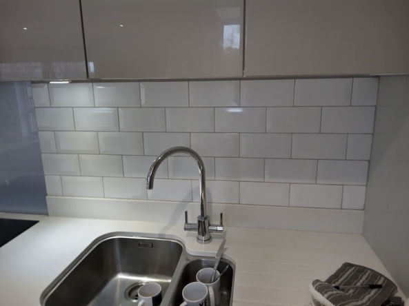 A kitchen tap, silver, with a silver sink, white tile backsplash