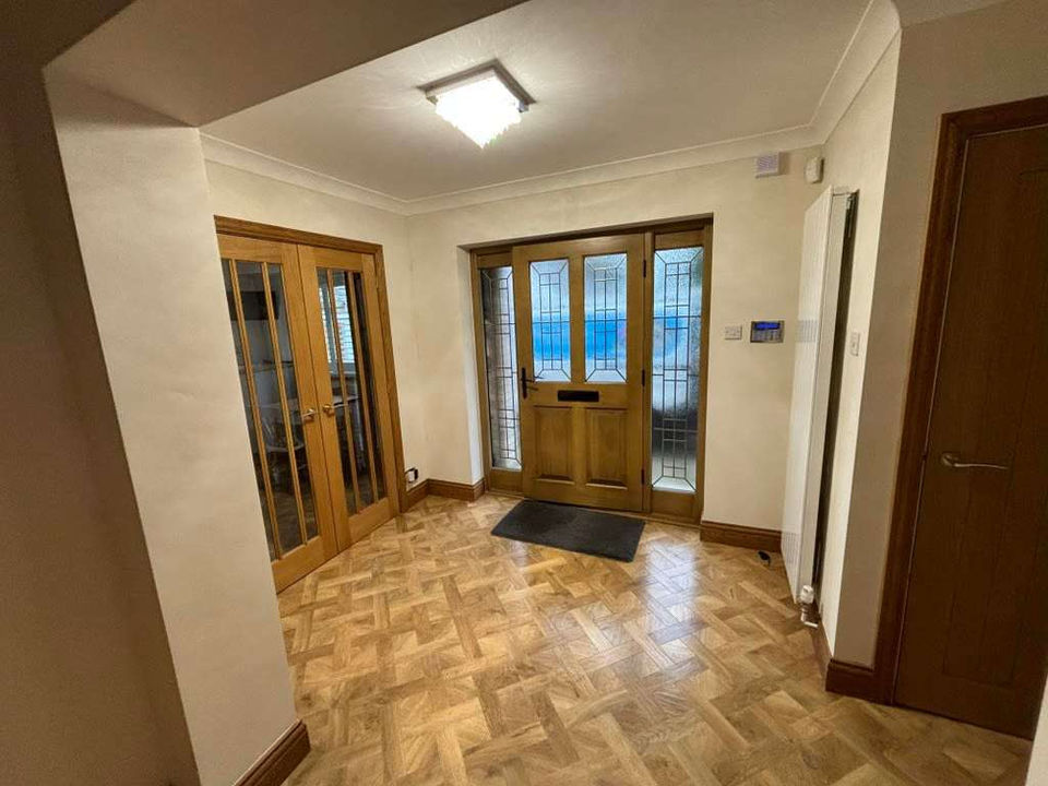An entrance hall to a home, wooden flooring, wooden doors with glass panes and white walls