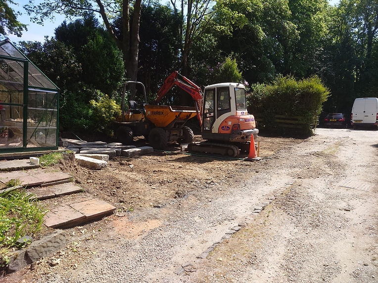 Compact excavator in a back garden, loading material into a dumper, trees in background
