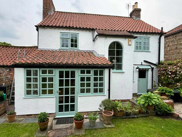Exterior view of a home from the back garden, nice green grass and plants, home is white with red tile roof