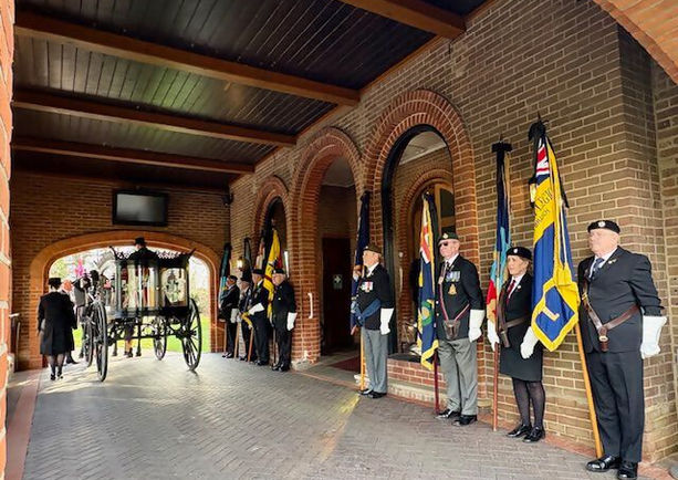 A horse and cart leaving a funeral procession with military guards stood in a line