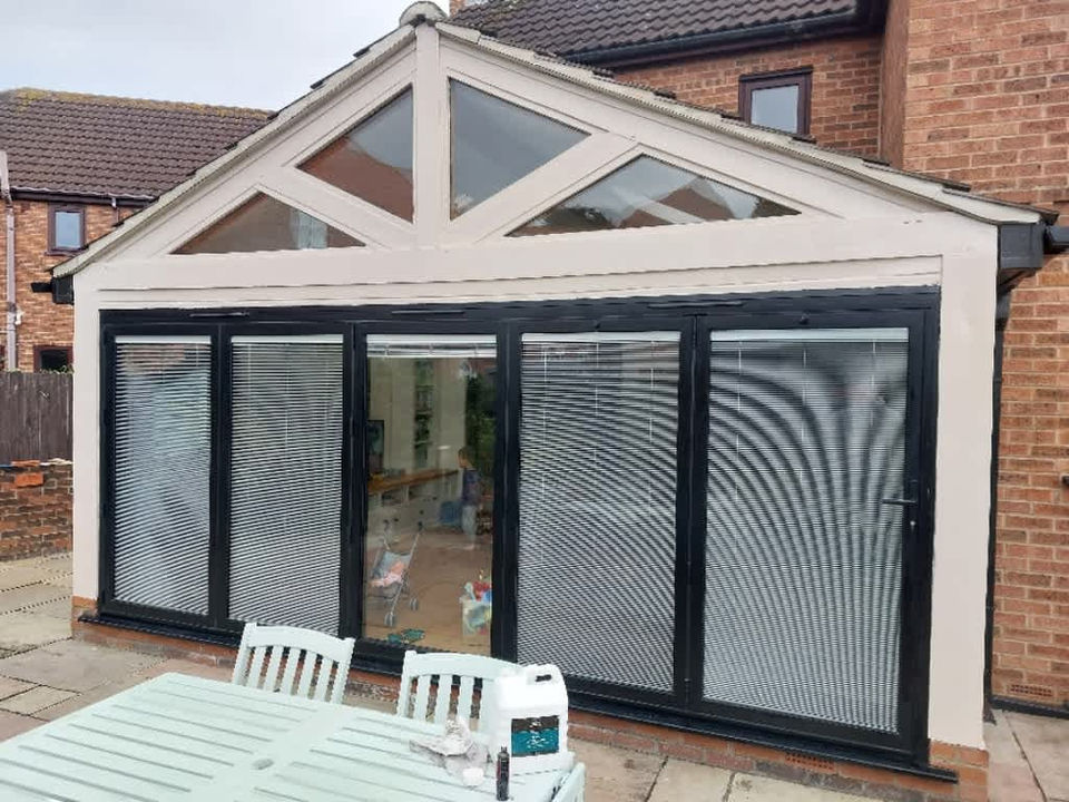 A large white conservatory, floor to ceiling windows with black trim and shutters 