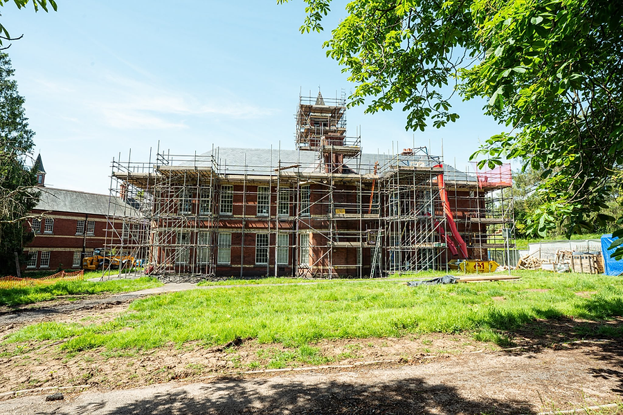 Scaffolding around a large house with green grass in front of it