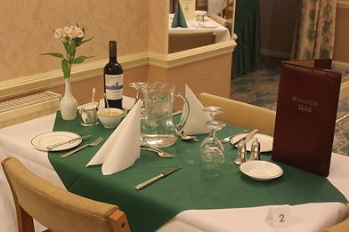 Elegant restaurant table set with green tablecloth, white napkins, wine bottle