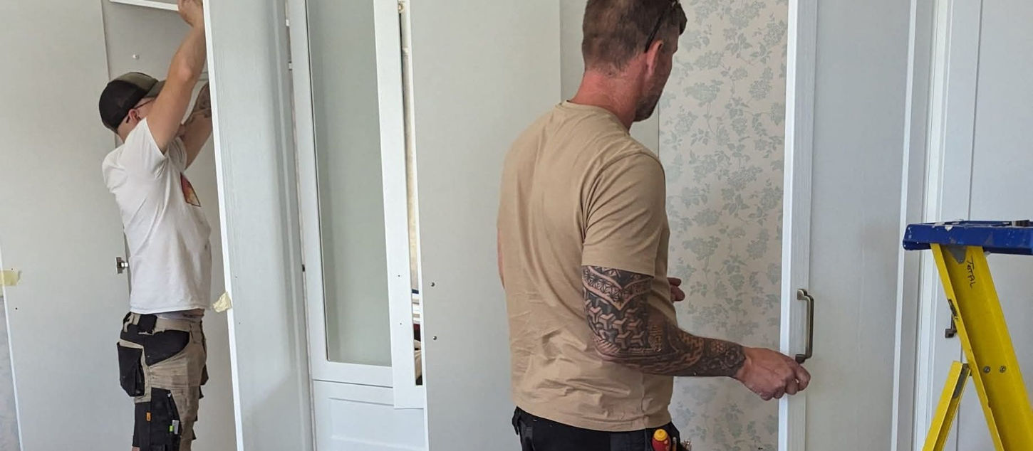 Two men installing white built-in wardrobes