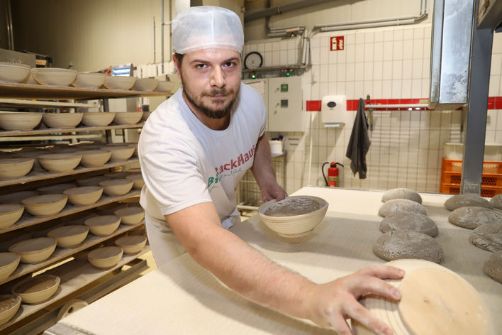 Ein junger Mann in Bäckerskleidung formt Brote in der Backstube