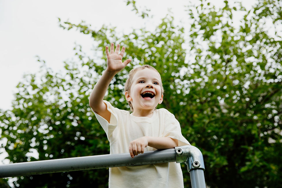 Young boy waving at the top of monkey bars
