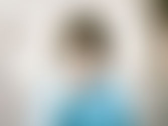 Child in a blue polka-dot jacket holds a magnifying glass, magnifying one eye. Neutral background, curious expression.