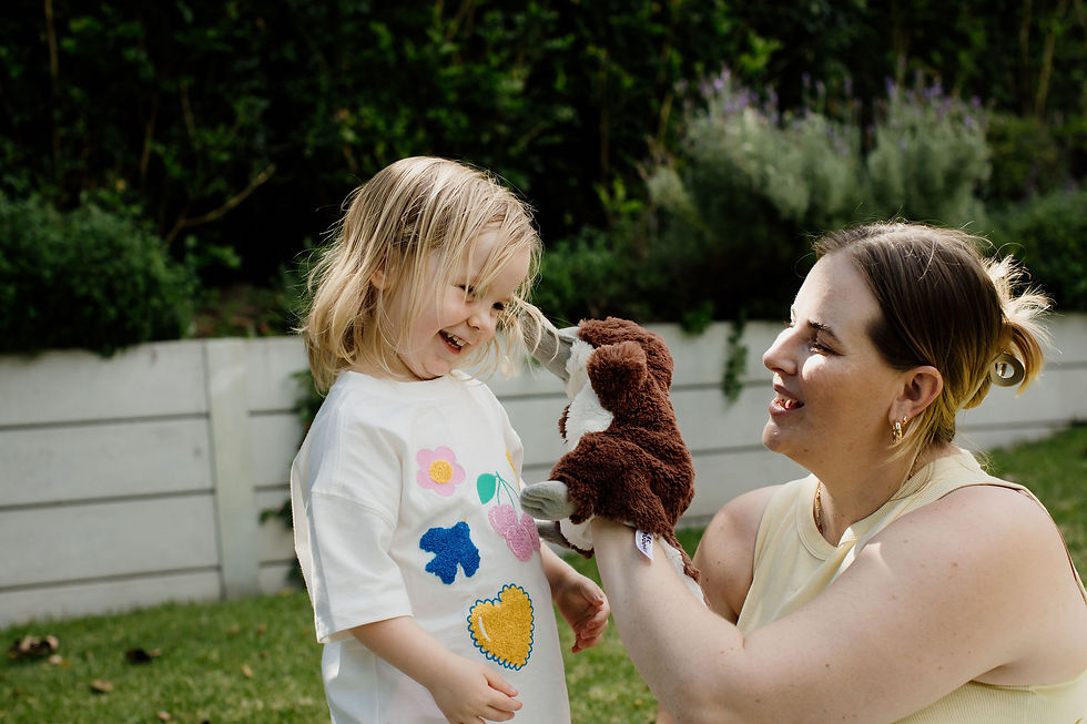 3 year old smiling and laughing at speech pathologist playing with puppet platypus in backyard