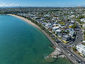 Aerial view of a long sandy beach, blue ocean, and coastal city.
