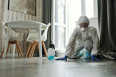 Biohazard cleanup technician in PPE cleaning an affected surface