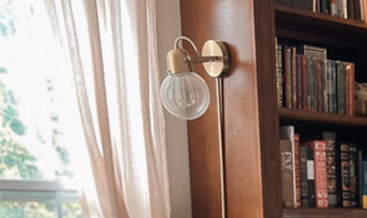 A light academia style bedroom has warmth filtering in through the large window across a vintage bed with a dark green plaid coverlet