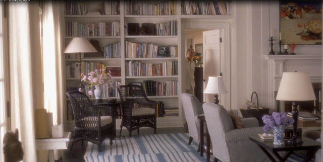 Cozy Nancy Meyers living room with bookshelves, wicker chairs, and lamps. A striped rug and flowers on tables add color. Bright, inviting atmosphere, from Something's Gotta Give.