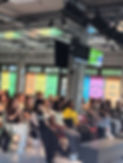 Audience at a tech event with diverse women, colorful banners, Women in Tech UK.