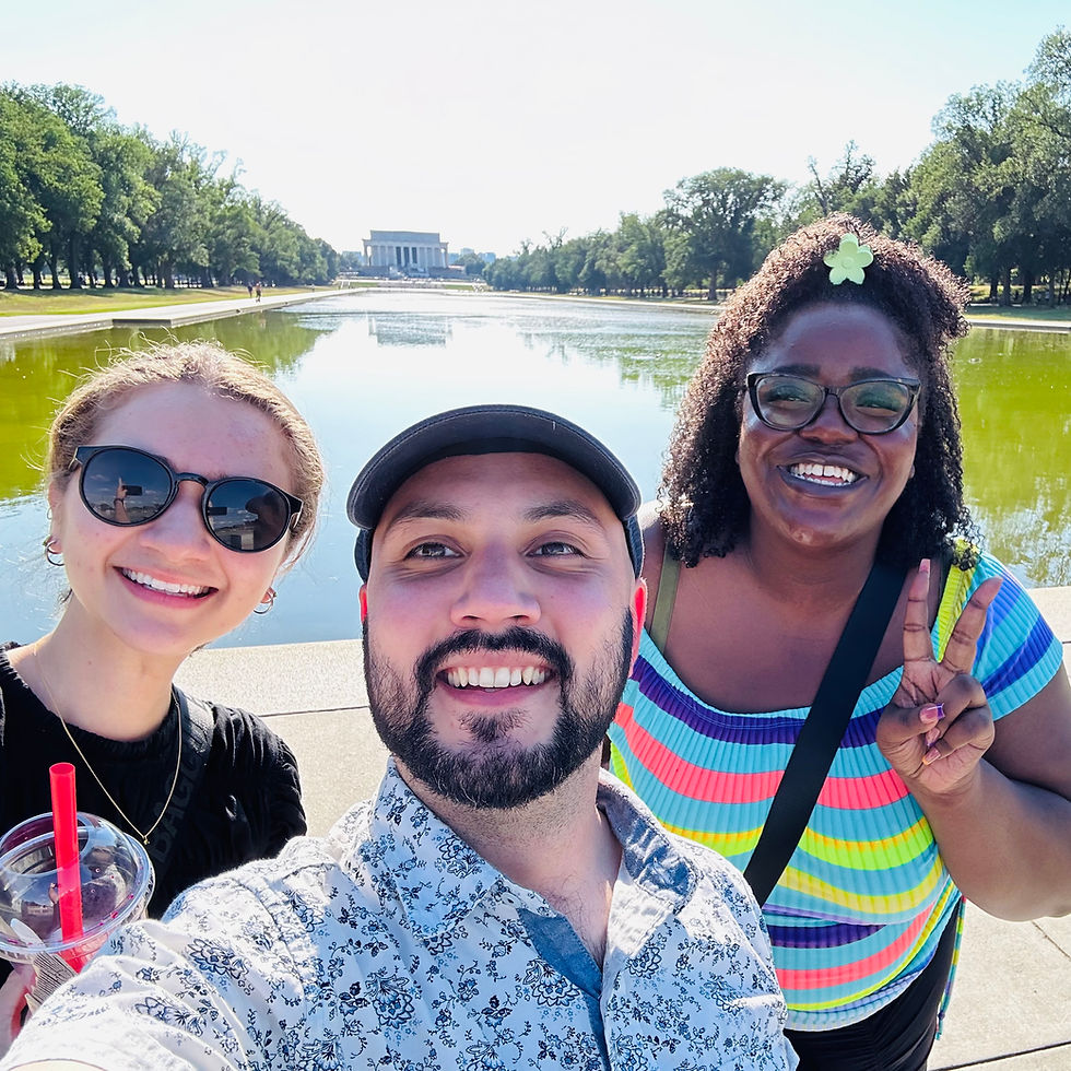 A group selfie of the author, a woman with light skin and hair pulled back wearing sunglasses, a man with light skin and a short black beard wearing a baseball cap, and a woman with dark skin and curly hair pulled into a yellow star clip shows the peace sign with her hand as they all smile in front of the reflecting pool in front of the Lincoln Memorial in Washington DC.