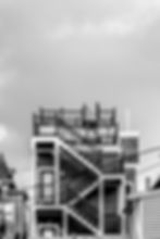 Black and white photo of a staircase zigzagging up the back of a multi-family home. Photo by CDMA on Unsplash.
