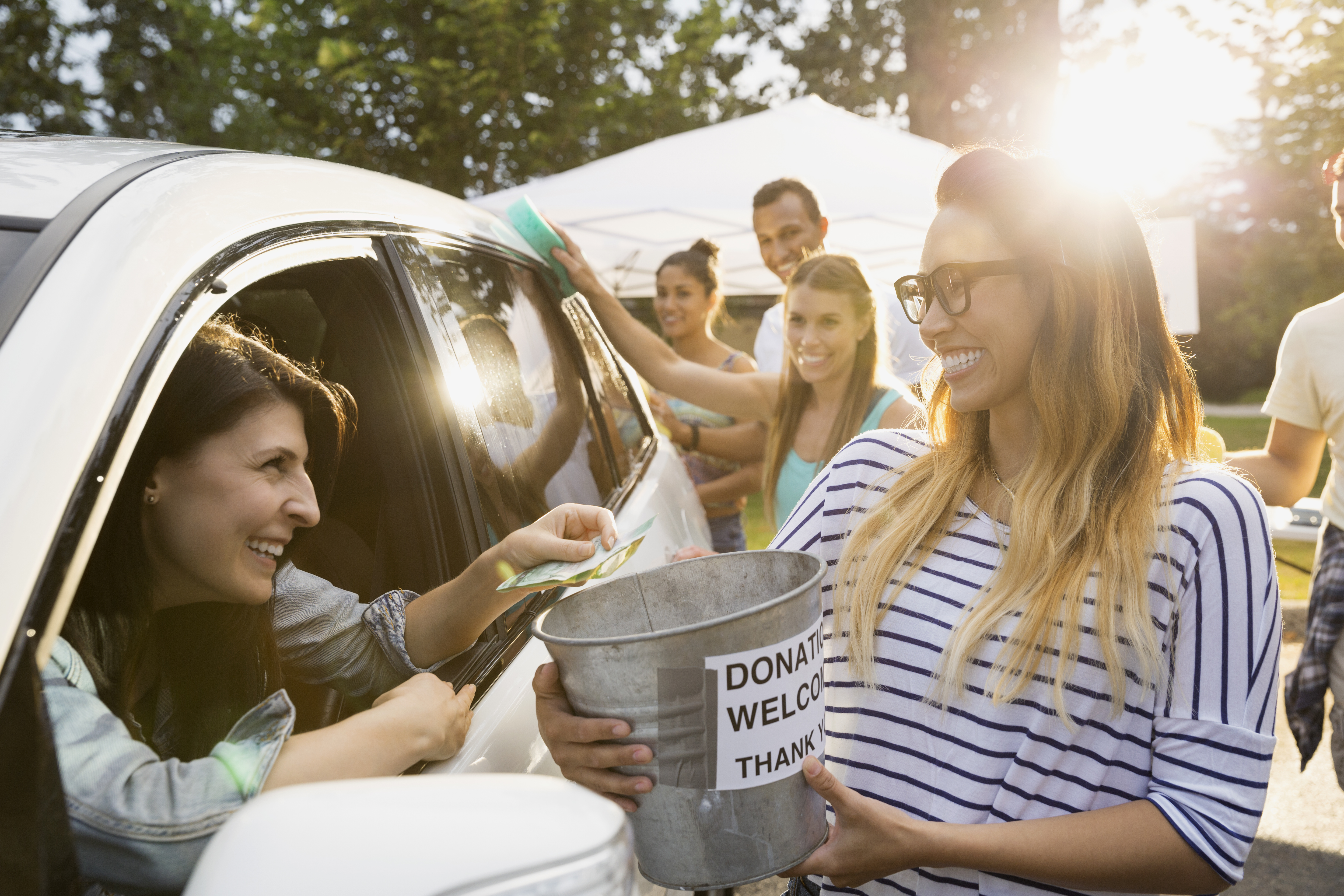 White woman in an SUV getting a carwash from three young people and making a donation to a young woman for their service