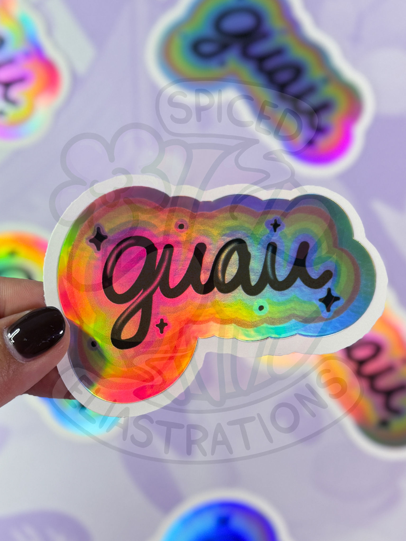 holographic sticker that reads "guau" surrounded by a rainbow bold border with black sparkles
