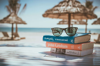 pile de livres posés sur une plage avec les lunettes de soleil par dessus.