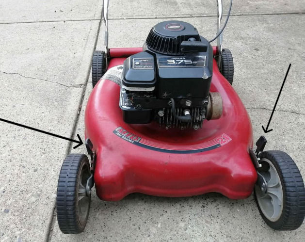 Red push lawn mower on concrete driveway, with arrows pointing to the cutting height adjustment levers