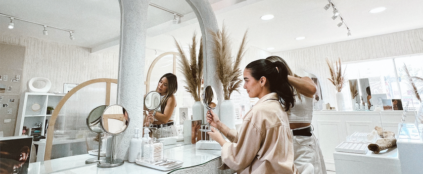 Mujer mirándose en el espejo mientras otra persona le arregla el cabello en salón.