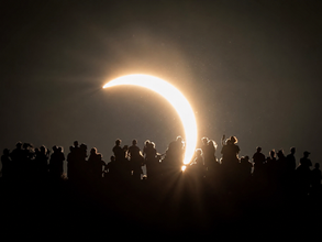 Partial solar eclipse viewed from Cley Hill in Somerset, with people silhouetted against the crescent sun.