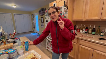 Woman in kitchen wearing glasses pointing, food and drinks on counter