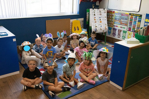 Children wearing Easter hats smiling together, sitting on a rug in classroom.