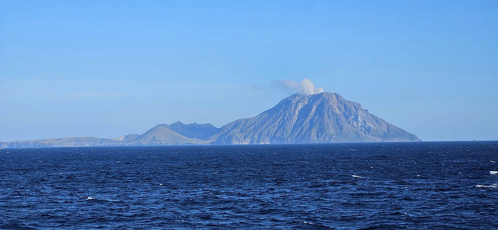 Mountain with small cloud of smoke in the blue ocean under clear sky.