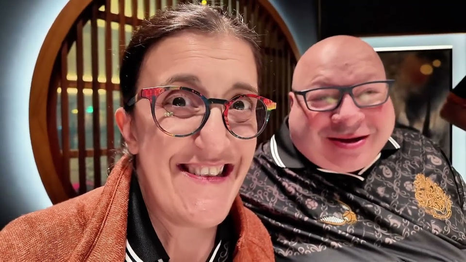 Lucia and Glynn, wearing glasses, smile happily at a restaurant About dinner.
