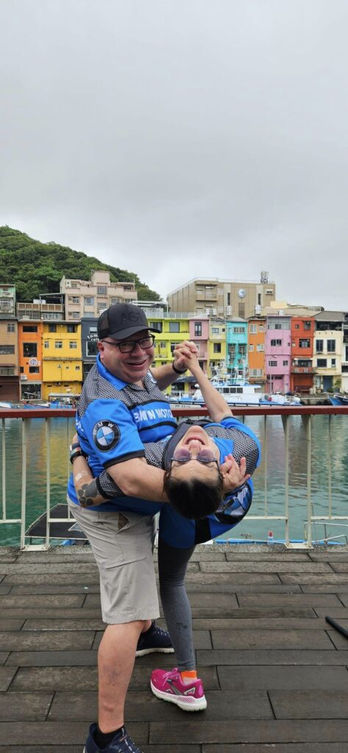 Two people dancing on a dock in front of colorful buildings, Lucia and Glynn.