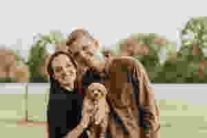 A photo of a family with their puppy in a green grassy field with trees.
