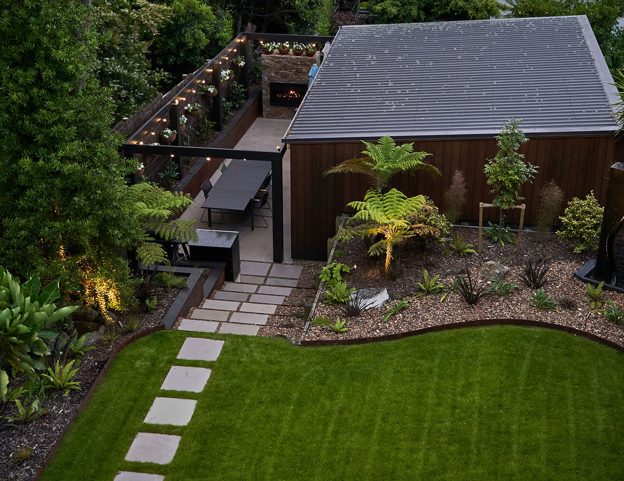 Backyard landscape with plants, patio, outdoor fireplace & dining.