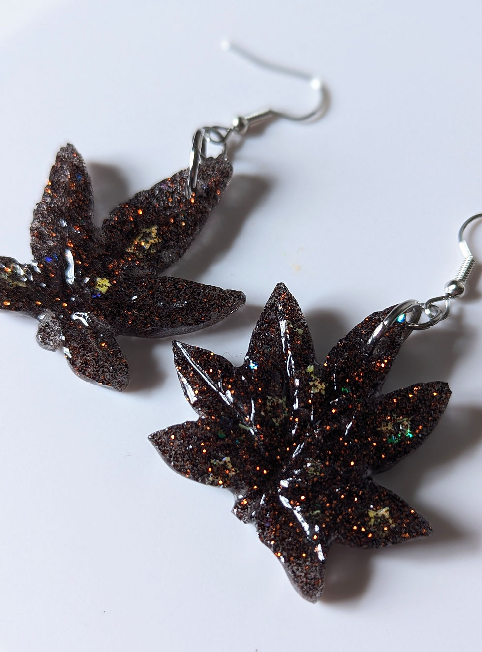 Thumbnail: Close up view of the Black Domina Hybrid Split Weed Leaf Earrings showing off their glittery details