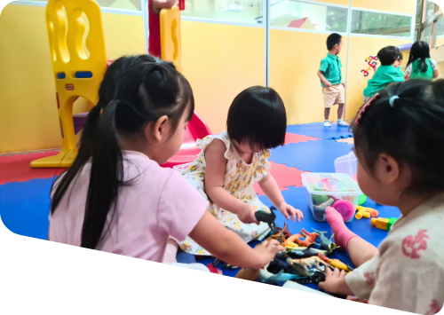 Group of kids playing with various toys on a soft floor mat in a playroom.