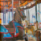 Oil painting of a close-up carousel horse with a blue-and-red saddle and other carousel horses behind it.
