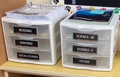 Two clear plastic drawer organizers on a desk, labeled Reading, Writing, Social Studies, Science-W, Science-S, and Other.