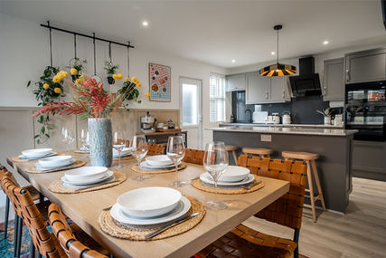 Open-plan dining and kitchen area with a wooden table set for six and grey built-in cabinets at Seaview Serviced Accommodation in the Wirral.
