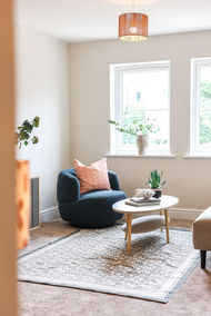 Staged seating corner in Huntingdon, York by WildKind Interiors – navy textured armchair with blush cushion, light wood oval coffee table with décor and potted succulent, on a patterned rug beneath bright windows.
