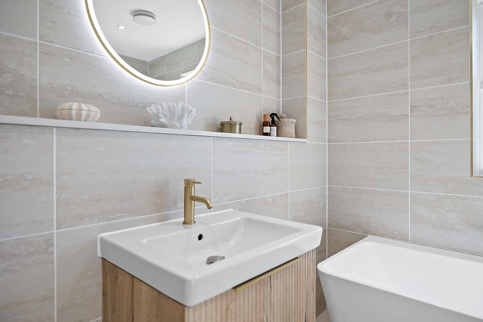 Modern beige-tiled bathroom with lit round mirror, white sink, gold faucet, and freestanding tub; calm, spa-like feel