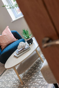Staged seating nook in Huntingdon, York by WildKind Interiors – light wood oval coffee table with coral sculpture, coffee-table books, and potted succulent, beside a navy armchair with blush cushion on a patterned rug.