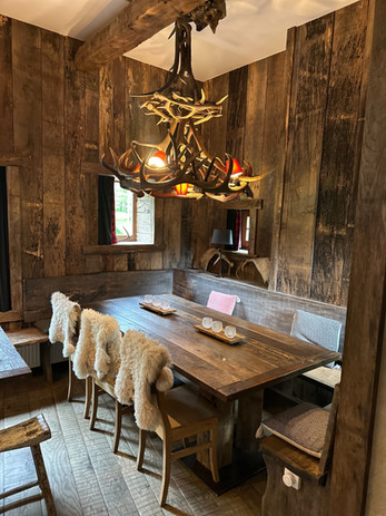 Houten eettafel met stoelen en groot licht in een rustieke kamer.