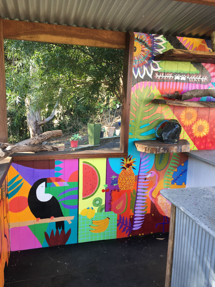 Tropical mural with toucan, fruit, and leaves painted on timber panels in a garden bar.