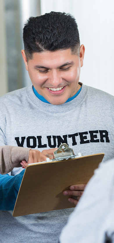 A man wearing a shirt that reads volunteer is smiling and looking at a clipboard.